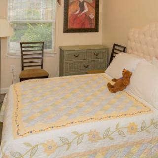 A cozy bedroom with a neatly made bed and a teddy bear placed on it, surrounded by tasteful decor and furniture.