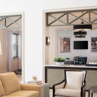 A modern living room with neutral tones featuring a sofa, armchair, and a TV in the background.