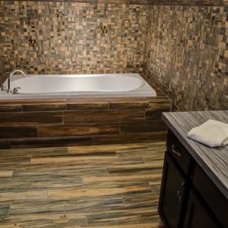 A modern bathroom featuring a white bathtub with mosaic tile walls and wood flooring.