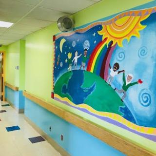 A vibrant mural adorning the hallway of a children's hospital, featuring whimsical elements like a rainbow and playful characters under a bright sun.