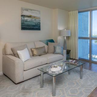 A cozy living room featuring a comfortable sofa, glass coffee table, and large window with curtains.