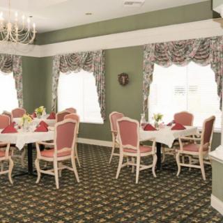 A formal dining room with elegantly set tables and chairs, featuring a chandelier and decorative curtains.