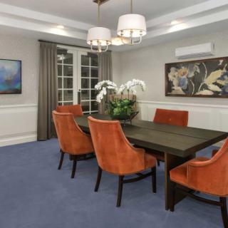 A modern dining room with orange chairs and a dark wood table, accented by a chandelier and artwork on the walls.