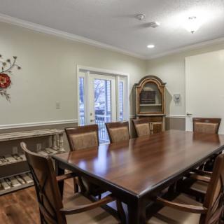 A well-furnished dining room with a large wooden table and chairs, featuring elegant decor and a cabinet in the background.
