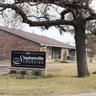 An apartment complex sign for Stephenville Crossing with surrounding buildings and trees.
