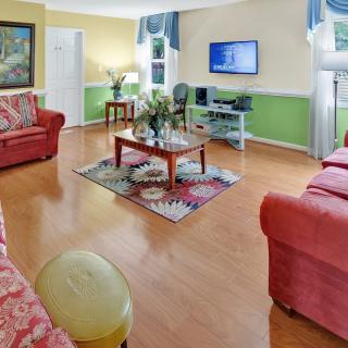 A cozy living room featuring red sofas, a wooden floor, and a wall-mounted television.