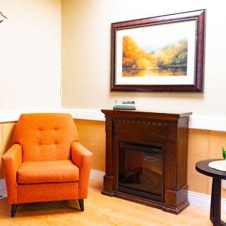 A cozy living room corner with an orange armchair, a wooden fireplace, and wall art.