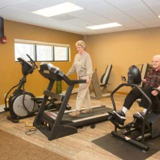 Senior adults exercising in a gym using a treadmill and stationary bike.
