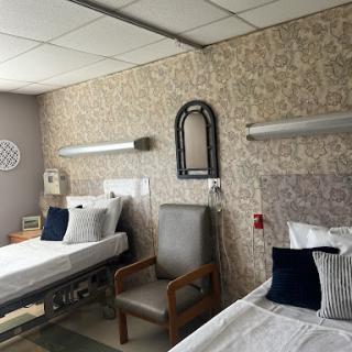 A well-designed hospital patient room featuring two beds, seated area, and a calming color scheme.