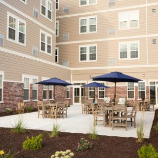 A well-furnished patio area with tables, chairs, and umbrellas in front of a multi-story building.
