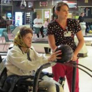 A person in a wheelchair receives assistance to bowl at an indoor facility.