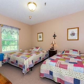A cozy bedroom with two single beds adorned with colorful quilts, featuring a window that lets in natural light and decorated walls with framed artwork.