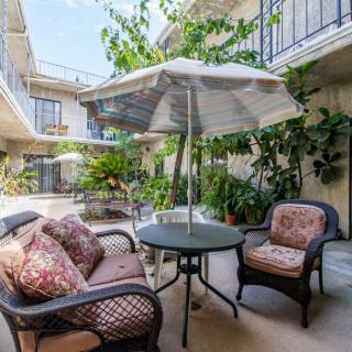A cozy patio area with cushioned chairs, a round table, and an umbrella surrounded by lush plants.