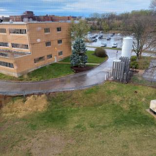 An aerial view of a building surrounded by greenery and a parking lot.