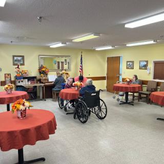 A cozy community dining area for residents, featuring tables set for gatherings and individuals engaging in conversation.