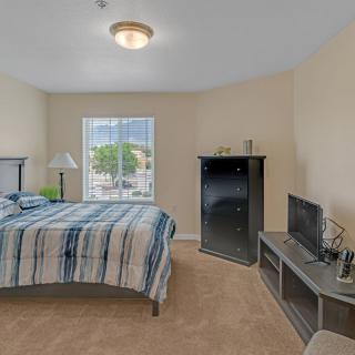 A well-lit bedroom with a striped bedspread, TV, and window view.