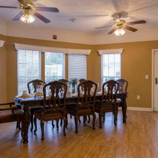 A spacious dining room with a wooden table and chairs, ceiling fans, and large windows.