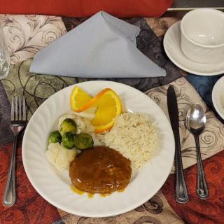 A well-arranged dinner plate featuring rice, gravy-covered meat, brussels sprouts, and a fruit garnish, set on an elegantly laid table.