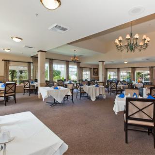 A spacious dining area with neatly arranged tables and chairs, featuring a chandelier and large windows.