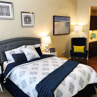 A cozy bedroom with elegant decor featuring a bed, decorative pillows, framed artwork on the walls, and soft lighting from table lamps.