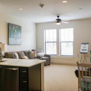 A bright and cozy living room with modern decor, featuring a large sofa, ceiling fan, and ample natural light from two windows.