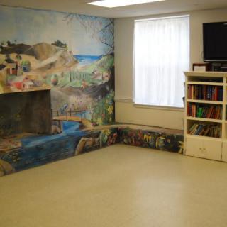 A room with a colorful mural, bookshelf, and TV.