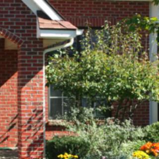 A charming brick house with a lush garden in front, featuring colorful flowers and a small tree.