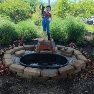 A charming garden fountain featuring a playful statue standing above a small pond, surrounded by lush greenery.