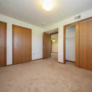 An empty bedroom with carpet flooring, wooden closet doors, and a ceiling light.