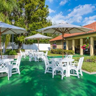 A sunny outdoor patio area with white tables and umbrellas set on a green surface.
