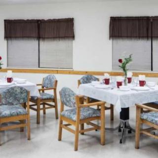 A dining room with several tables and chairs, each table set with white tablecloths and small flower arrangements.