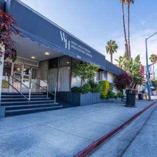 A view of a modern building entrance with palm trees lining the street.