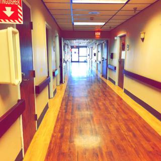 A hospital corridor with wooden flooring and a bright exit in the distance.