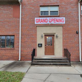 A brick building with a 'Grand Opening' sign above the entrance.