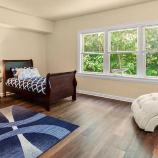 A minimalistic bedroom with a single bed, large window, and wooden flooring.