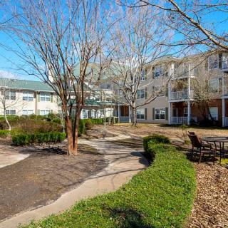 A well-maintained apartment complex courtyard featuring a pathway, trees, and benches.