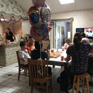 A family gathering around a table celebrating with balloons and food.