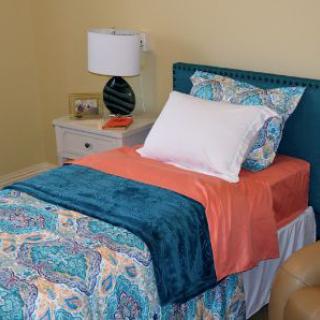 A cozy bedroom with a single bed featuring colorful bedding and a nearby nightstand with a lamp.