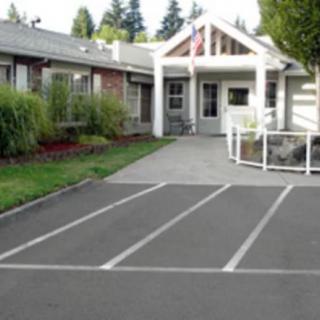 A small building with an entrance, surrounded by landscaped greenery and adjacent to a parking area.