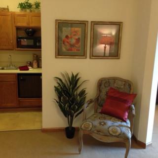 A cozy living area with a decorative chair and wall art next to a small kitchen.