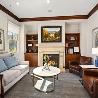 A stylish living room featuring a cozy fireplace, with a sofa and armchair arranged around a modern coffee table. The space is adorned with artwork above the fireplace and bookshelves on either side.