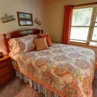 A cozy bedroom with a neatly made bed and patterned bedding, complemented by warm-colored curtains and natural light streaming through the window.