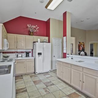 A modern kitchen with white cabinets, a red accent wall, and tile flooring.