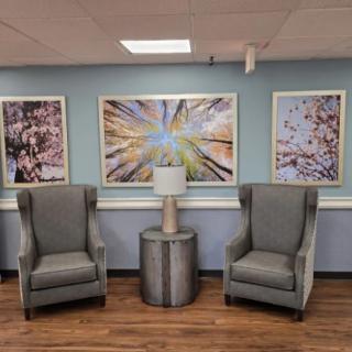 A cozy waiting area with two gray armchairs flanking a small round table, set against a wall adorned with abstract artwork.