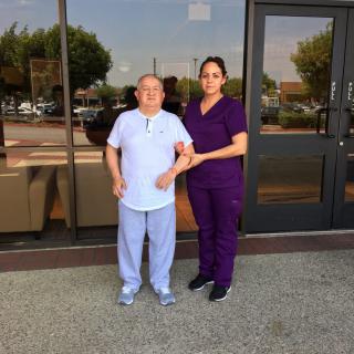A nurse and an elderly patient standing outside a building.