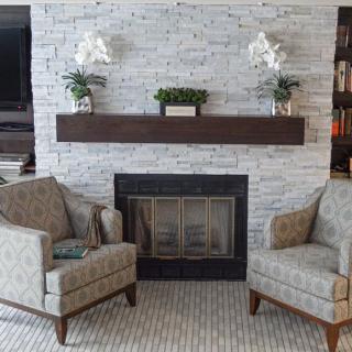 A cozy living room with a stone fireplace, two armchairs, and decorative plants on the mantel.