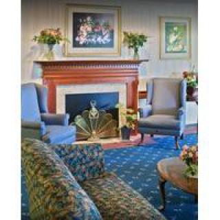 A cozy living room featuring a fireplace, elegant armchairs, and a sofa, adorned with artwork and floral decor.