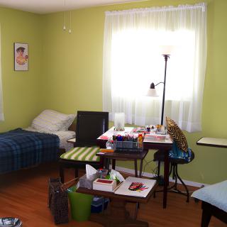 A small bedroom with a single bed and a cluttered desk under a window.