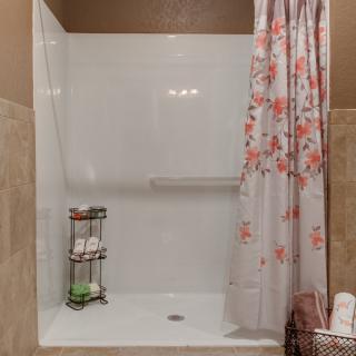 A clean and organized bathroom shower with a floral curtain and neatly arranged bath products.