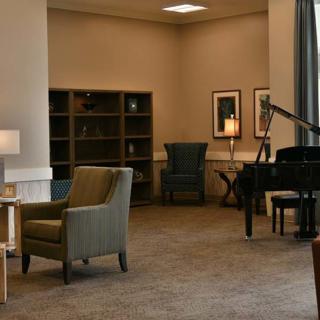 A cozy lounge area featuring a piano, armchairs, and bookshelves.